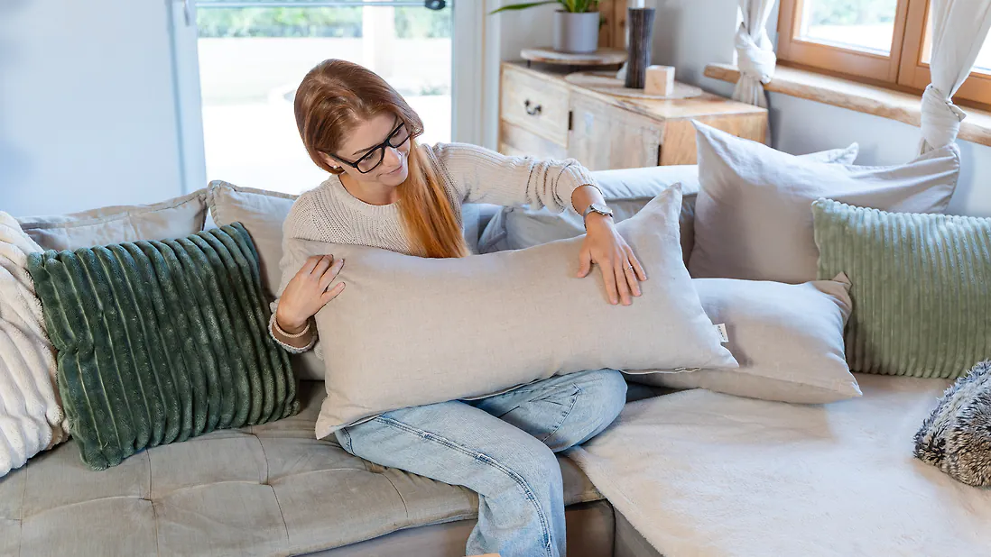 Frau auf Sofa h&auml;lt Zirbenschlafkissen 40x80cm mit Leinenbezug