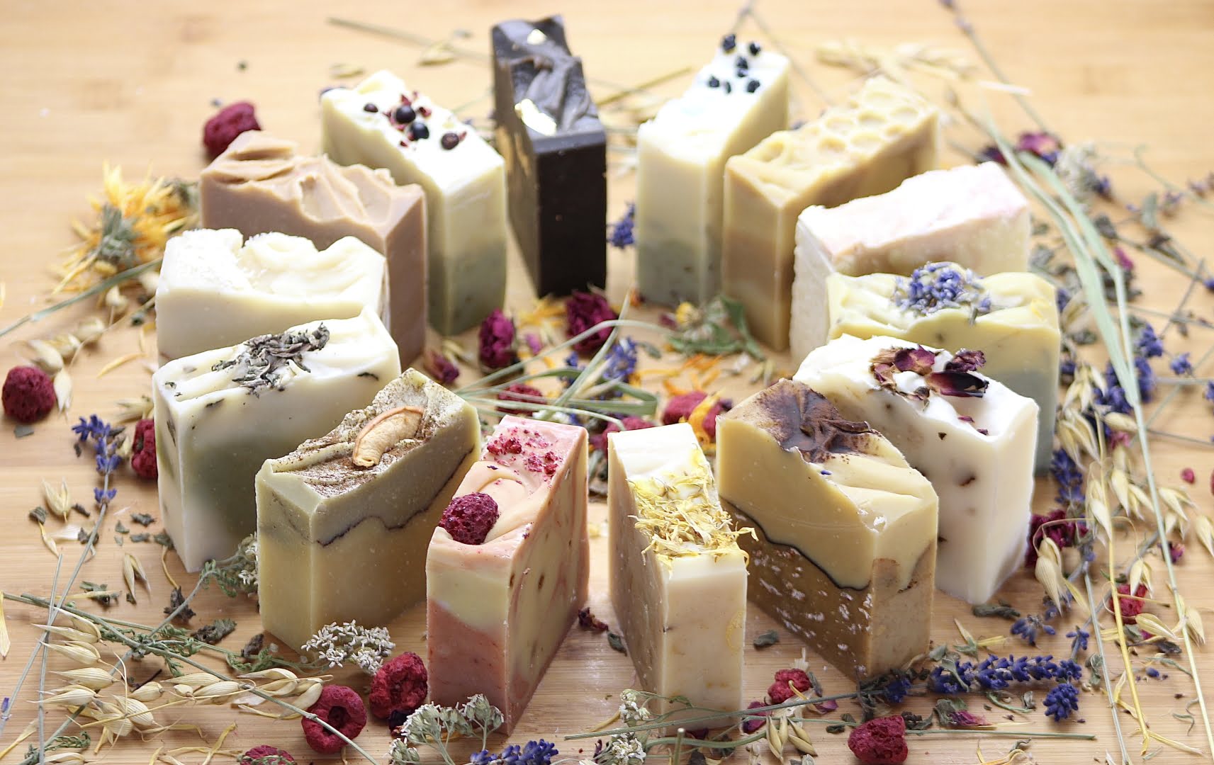 Verschiedene Naturseifen in einem Kreis aufgestellt, mit Blumen und Kr&auml;utern im Hintergrund.